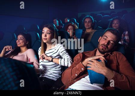 Groupe de personnes regardant le film au cinéma, fille réveille le petit ami endormi. Banque D'Images