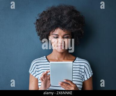 Femme africaine, étudiante et tablette en studio pour lire, penser ou étudier sur APP pour tester par fond bleu. Personne, fille et cliquez sur numérique Banque D'Images