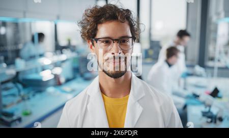 Laboratoire des sciences médicales : portrait d'un beau jeune scientifique latin portant un manteau blanc souriant regardant la caméra. Jeune spécialiste de la recherche en biotechnologie. Portrait gros plan moyen Banque D'Images