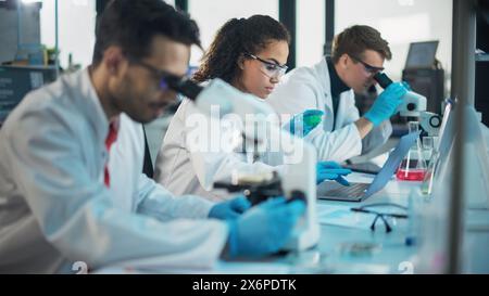 Laboratoire des sciences médicales : rangée de l'équipe diversifiée de jeunes scientifiques multiethniques regardant sous microscope, analyser les produits chimiques, parler, résoudre des problèmes. Spécialistes en biotechnologie travaillant dans Advanced Lab Banque D'Images
