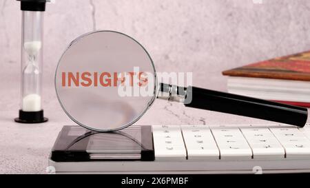 Concept Insight. APERÇOIT le mot à travers une loupe sur une calculatrice avec un sablier et un livre en arrière-plan sans mise au point Banque D'Images