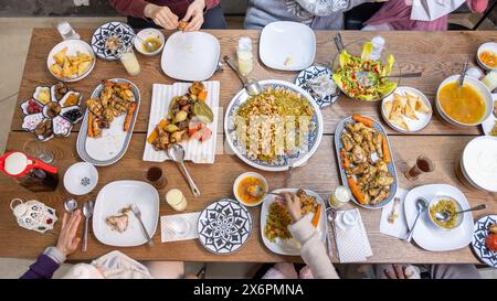 Une famille musulmane se réunit autour d'une table rectangulaire, partageant ensemble un repas réconfortant, avec des membres de différents âges ajoutant à la chaleur et à la joie de Banque D'Images