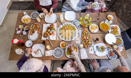 Une famille musulmane se réunit autour d'une table rectangulaire, partageant ensemble un repas réconfortant, avec des membres de différents âges ajoutant à la chaleur et à la joie de Banque D'Images