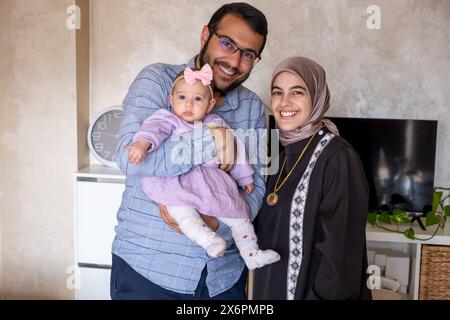 portrait pour jeune famille avec leur premier bébé la tenant et regardant la caméra vêtue de beaux vêtements Banque D'Images