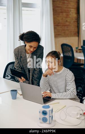 Deux collègues féminines concentrées travaillant sur le projet ensemble et utilisent un ordinateur portable assis dans le bureau Banque D'Images
