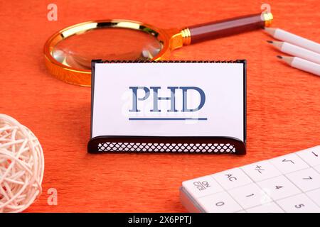 Word PhD. Docteur en philosophie. PHD sur une carte de visite blanche sur une surface orange Banque D'Images