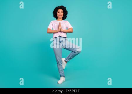 Photo de Dreaming Girl en t shirt rose et Jean vêtement élégant stand une jambe méditation pose isolé sur fond de couleur cyan Banque D'Images