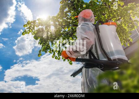 Jardinier en costume de protection pulvérisant arbre avec pulvérisateur. Banque D'Images