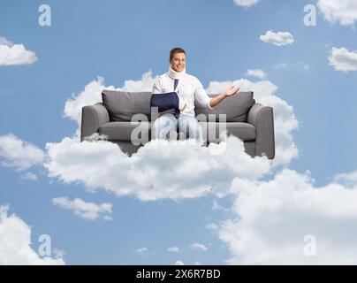 Jeune homme avec un bras cassé et une attelle de cou assis sur un canapé et flottant sur un nuage dans le ciel Banque D'Images