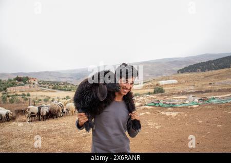 Jeune adolescent arabe tenant de petits moutons se sentant heureux et remerciant Dieu pour ses dons dans le désert Banque D'Images