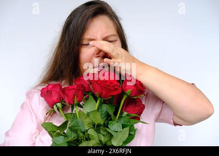 bouquet de fleurs, roses rouges, femme d'âge moyen 50 ans avec des allergies avec les yeux gonflés de l'étonnement et de la surprise, allergie au pollen de fleur, Banque D'Images