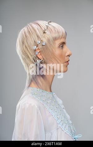 Portrait de profil latéral de jeune femme - cheveux blonds, reflets violets - piercing septum, boucles d'oreilles multiples, dessus floral transparent, tête de feuille d'argent Banque D'Images