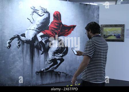 New York, New York, États-Unis. 15 mai 2024. Un homme prend une photo d'une œuvre subvertie peinte à l'origine par Jacques-Louis David (1748-1825)-Bonaparte traversant le Grand col du Saint Bernard 2018 Avenue de Flandre, Paris, France, vue lors de l'ouverture du nouveau Banksy Museum situé au 277 canal Street dans le Lower Manhattan. Plus de 160 œuvres de Banksy ont été recréées par 10 artistes anonymes, car toutes les œuvres sauf une n'existent plus. (Crédit image : © Nancy Kaszerman/ZUMA Press Wire) USAGE ÉDITORIAL SEULEMENT! Non destiné à UN USAGE commercial ! Banque D'Images