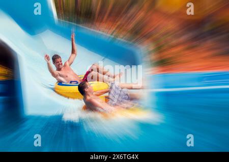 Flou radial de deux jeunes hommes glissant ensemble dans le parc aquatique Acqua plus. Crète, Grèce. Banque D'Images