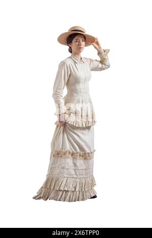 Jeune femme avec la main sur le bord du chapeau de paille portant une robe vintage beige des années 1880 isolé sur blanc Banque D'Images