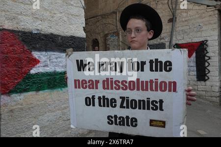 JÉRUSALEM - 14 MAI : membre de Neturei Karta, un mouvement juif ultra-orthodoxe marginal au sein du bloc anti-sioniste tient un panneau qui dit "nous prions pour la quasi dissolution de l'État sioniste" alors qu'il se tient à côté de drapeaux palestiniens peints sur les murs lors d'un rassemblement contre la création de l'État d'Israël dans le quartier religieux de Mea Shearim alors qu'Israël célèbre le 76ème jour de l'indépendance, au milieu des combats continus entre Israël et le groupe militant Hamas dans la bande de Gaza le 14 mai 2024 à Jérusalem. Neturei Karta s'oppose au sionisme et appelle à un "démantèlement pacifique" de l'Etat Banque D'Images