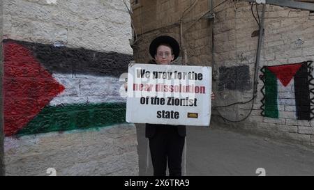 JÉRUSALEM - 14 MAI : membre de Neturei Karta, un mouvement juif ultra-orthodoxe marginal au sein du bloc anti-sioniste tient un panneau qui dit "nous prions pour la quasi dissolution de l'État sioniste" alors qu'il se tient à côté de drapeaux palestiniens peints sur les murs lors d'un rassemblement contre la création de l'État d'Israël dans le quartier religieux de Mea Shearim alors qu'Israël célèbre le 76ème jour de l'indépendance, au milieu des combats continus entre Israël et le groupe militant Hamas dans la bande de Gaza le 14 mai 2024 à Jérusalem. Neturei Karta s'oppose au sionisme et appelle à un "démantèlement pacifique" de l'Etat Banque D'Images