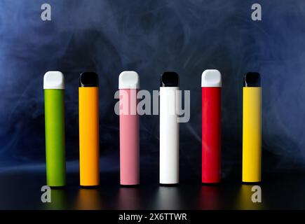 Ensemble de cigarettes électroniques jetables colorées sur un fond noir avec de la fumée. Le concept de tabagisme moderne, vapotage et nicotine Banque D'Images