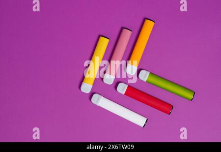 Cigarettes électroniques jetables colorées sur un fond violet. Le concept de tabagisme moderne, vapotage et nicotine. Vue de dessus Banque D'Images