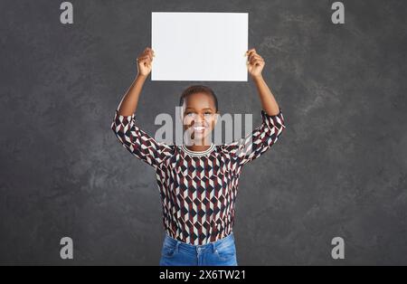 Positive joyeuse femme afro-américaine démontre une bannière blanche avec un espace pour le texte. Banque D'Images