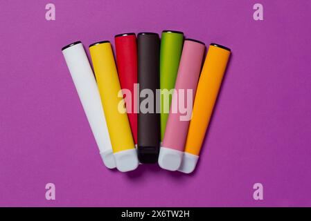 Ensemble de cigarettes électroniques jetables colorées sur un fond violet. Le concept de tabagisme moderne, vapotage et nicotine. Vue de dessus. Banque D'Images