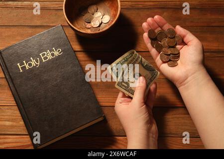 Donnez et donnez concept. Femme avec de l'argent, gros plan. Bible et bol de pièces de monnaie sur la table en bois, vue de dessus Banque D'Images