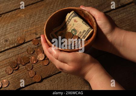 Donnez et donnez concept. Femme tenant un bol avec des pièces de monnaie et des billets de dollar à la table en bois, gros plan Banque D'Images