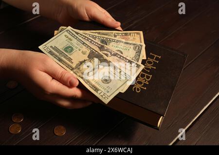 Donnez et donnez concept. Femme avec des billets de banque en dollars, des pièces de monnaie et la Bible à la table en bois, gros plan Banque D'Images