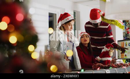 Gestionnaire dans le bureau décoré de Noël délégant des tâches aux membres du personnel avant la saison des vacances d'hiver. Directeur enseignant aux employés comment terminer correctement le projet dans l'espace de travail de Noël ornent Banque D'Images