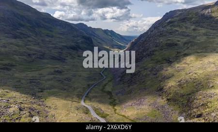 Vue aérienne d'une route sinueuse traversant une vallée de montagne verdoyante sous un ciel nuageux Banque D'Images