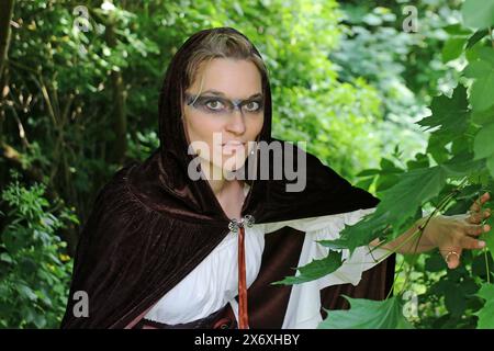 Une femme comme une chasseuse médiévale dans une robe avec une capuche se cache dans la forêt Banque D'Images