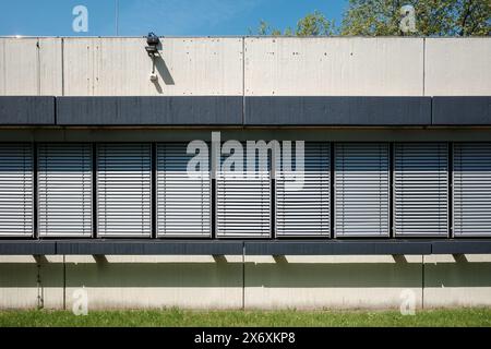 Ensoleillé et extérieur d'un bâtiment industriel moderne avec des volets métalliques élégants et une façade minimaliste en béton. Banque D'Images