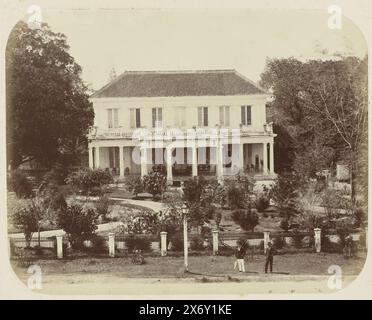 La maison de résidence à Surabaya, la maison de résidence à Surabaya vue de face. En face de la maison, il y a un grand jardin et une grande véranda avec un certain nombre de chaises et une horloge sur la droite qui montre cinq et deux. Deux Européens se tiennent devant la porte de la rue. Une partie de l'album photo présenté par l'Association Soerabayasche des fabricants de sucre à Frederik Beyerinck, résident de Soerabaya., photographie, Herman Salzwedel, Soerabayasche Vereeniging van Suikerfabrikanten, Surabaya, 1876 - 1884, support photographique, tirage à l'albumine, hauteur, 22,3 cm × largeur, 27,8 Banque D'Images