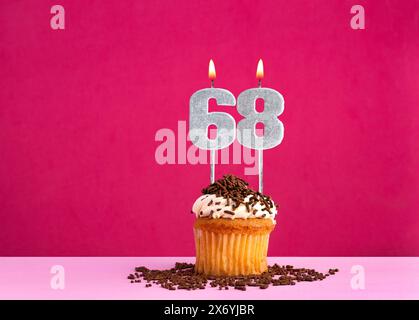 Célébration d'anniversaire avec numéro de bougie 68 - cupcake au chocolat sur fond rose Banque D'Images