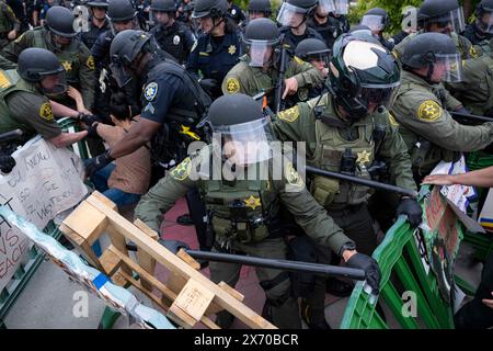 Irvine, Californie, États-Unis. 1er janvier 2023. Les agents du SWAT franchissent la barrière du campement tout en emmenant un manifestant en détention pour être arrêté. Des agents de nombreux services de police autour du comté d'Orange, en Californie, ont été appelés sur le campus d'Irvine de l'Université de Californie (UC) pour nettoyer un campement palestinien en pleine expansion prenant le contrôle du centre de l'Université. Les étudiants se barricadèrent en cercle, fortifiant leur périmètre avec des palettes de bois et divers autres objets pour empêcher les autorités d'entrer. Au total, 50 manifestants ont été arrêtés et le campement a été achevé Banque D'Images