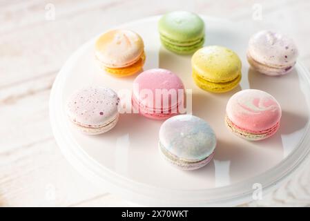 Macarons multicolores illuminés par les rayons du soleil projetant leur ombre, sur fond de bois clair, mise au point sélective. Banque D'Images