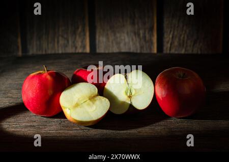 Quatre pommes rouges polies sur fond rustique, dont une coupée en deux, révélant une chair juteuse. Fruits frais naturels parfaits pour favoriser une alimentation saine Banque D'Images