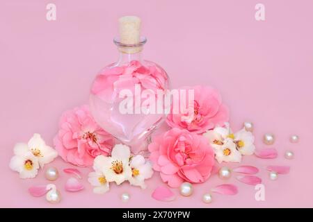 Parfum de fleur de rose et d'oranger dans une bouteille en forme de coeur sur rose avec des fleurs et des perles en vrac. Cadeau de produit de beauté floral. Banque D'Images