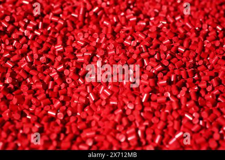 Cadre macro de granulés de plastique rouge. Le composite polymère est versé dans un réservoir pour la production ultérieure et le coulage dans des moules spéciaux. Banque D'Images