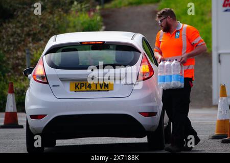 Les gens ramassent de l'eau en bouteille au parking Freshwater à Brixham. Environ 16 000 ménages et entreprises de la région de Brixham, dans le Devon, ont été priés de ne pas utiliser leur eau du robinet pour boire sans la faire bouillir et la refroidir d’abord, suite à la découverte de petites traces d’un parasite dans le réseau d’eau local. Date de la photo : vendredi 17 mai 2024. Banque D'Images