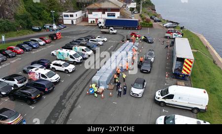 Une vue par drone de gens qui ramassent de l'eau en bouteille au parking Freshwater à Brixham. Environ 16 000 ménages et entreprises de la région de Brixham, dans le Devon, ont été priés de ne pas utiliser leur eau du robinet pour boire sans la faire bouillir et la refroidir d’abord, suite à la découverte de petites traces d’un parasite dans le réseau d’eau local. Date de la photo : vendredi 17 mai 2024. Banque D'Images