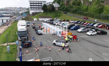 Une vue par drone de gens qui ramassent de l'eau en bouteille au parking Freshwater à Brixham. Environ 16 000 ménages et entreprises de la région de Brixham, dans le Devon, ont été priés de ne pas utiliser leur eau du robinet pour boire sans la faire bouillir et la refroidir d’abord, suite à la découverte de petites traces d’un parasite dans le réseau d’eau local. Date de la photo : vendredi 17 mai 2024. Banque D'Images