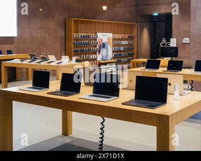 Paris, France - 23 décembre 2024 : un Apple Store présentant des ordinateurs portables MacBook sur des tables en bois, avec des étagères de coques iPhone et d'autres accessoires Apple affichés en arrière-plan. Banque D'Images