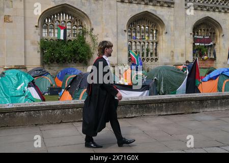 Un étudiant diplômé marche près d'une manifestation de campement sur le conflit de Gaza sur le terrain de l'Université de Cambridge. Les cérémonies de remise des diplômes ont été déplacées en raison du camp de protestation pro-palestinien. Date de la photo : vendredi 17 mai 2024. Banque D'Images