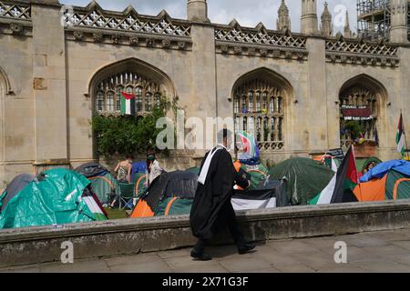 Un étudiant diplômé marche près d'une manifestation de campement sur le conflit de Gaza sur le terrain de l'Université de Cambridge. Les cérémonies de remise des diplômes ont été déplacées en raison du camp de protestation pro-palestinien. Date de la photo : vendredi 17 mai 2024. Banque D'Images