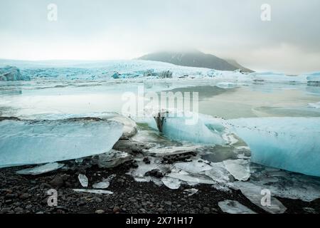 Vue d'un iceberg bleu détaché de la langue du glacier de Fjallsjökull dans la lagune glaciaire de Fjallsárlón en Islande par une journée nuageuse. Avec une vue de Banque D'Images