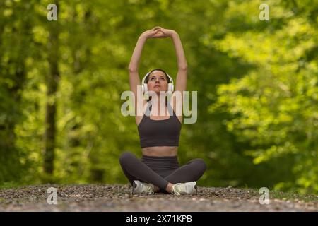 Femme sportive faisant des exercices d'étirement à l'extérieur dans le parc, écoutant de la musique avec des écouteurs. Banque D'Images