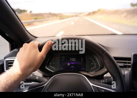 Vue du conducteur sur le compteur de vitesse à 100 km/h, avec la main sur le volant. Vue du jour de l'intérieur d'une voiture de conducteur POV à paysage de route floue. Banque D'Images