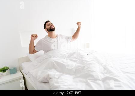 Photo du gars de bonne humeur positive réveillé dans les poings étirés du matin dans la maison de chambre Banque D'Images