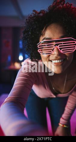 Écran vertical : diverse multiethnique jeune femme noire dansant dans des lunettes futuristes néon luisantes, ayant une fête à la maison dans un appartement loft. Enregistrement de vidéos virales drôles pour les médias sociaux. Banque D'Images